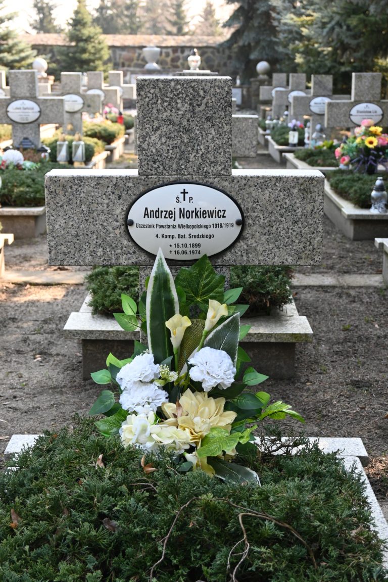 Krzyż z tabliczką imienia i nazwiska powstańca Andrzeja Norkiewicza z dużym bukietem kwiatów na kwaterze powstańców w Środzie Wielkopolskiej.