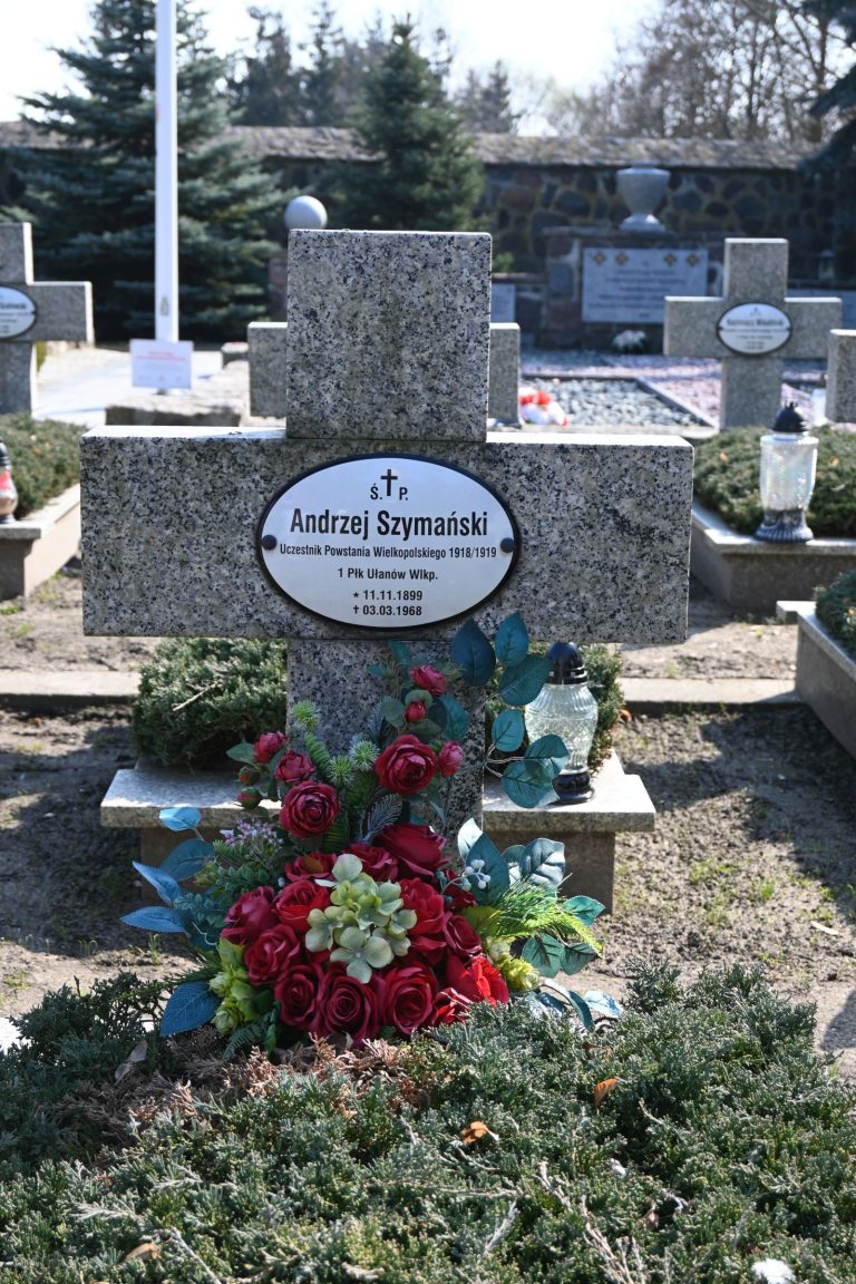 Krzyż z tabliczką imienia i nazwiska powstańca Andrzeja Szymańskiego ozdobiony kwiatami na kwaterze powstańców w Środzie Wielkopolskiej.