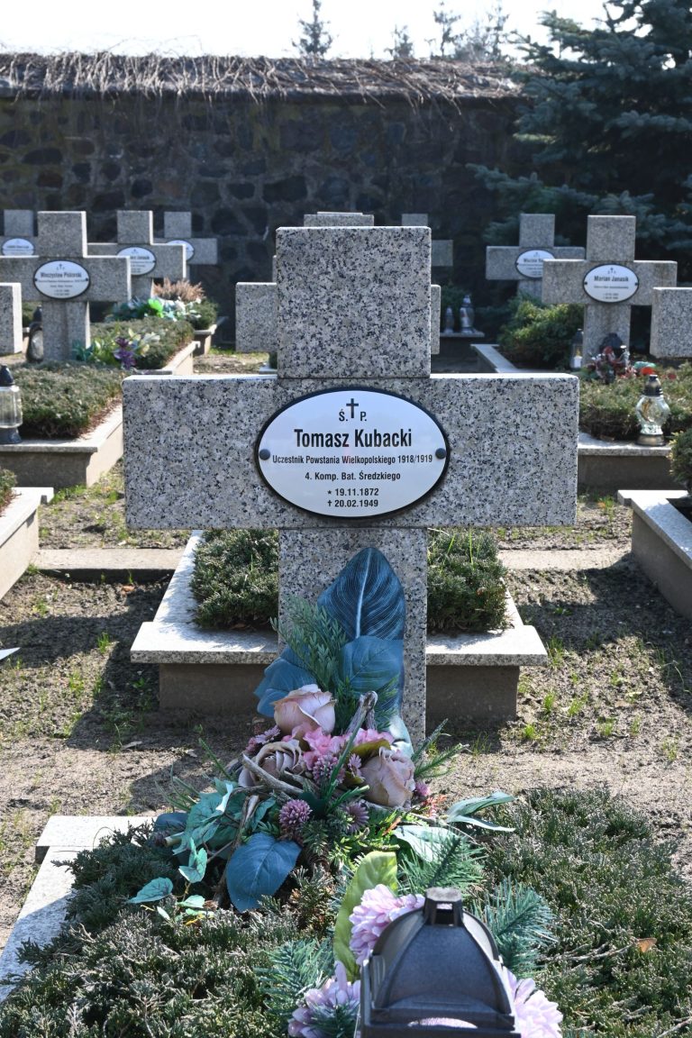 Nagrobek Tomasza Kubackiego w Kwaterze Powstańców Wielkopolskich – betonowy krzyż z tabliczką z imieniem; przed nim kolorowy wieniec z różowymi i zielonymi kwiatami